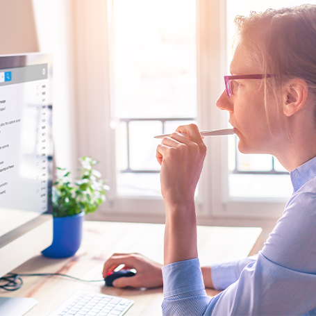 Frau am Schreibtisch schaut konzentriert in Monitor und hat Stift in der Hand