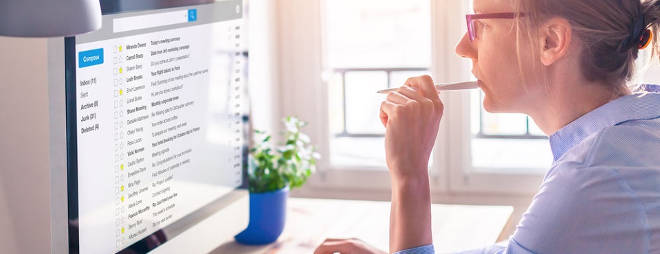 Frau am Schreibtisch schaut konzentriert in Monitor und hat Stift in der Hand